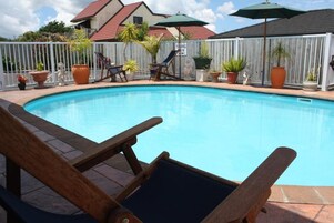 A swimming pool with lounge chairs and umbrellas, surrounded by a white fence and potted plants.