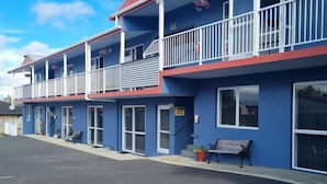 Um motel de dois andares com teto vermelho, grades brancas e estacionamento em frente.