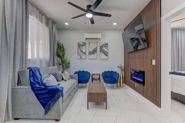 Un salon moderne avec un canapé gris, des fauteuils bleus, une table basse en bois et un téléviseur à écran plat fixé à un mur en bois.