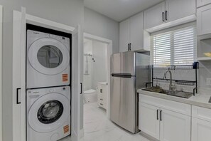 A modern kitchen with a stainless steel refrigerator, a built-in washing machine, and a sink with a drying rack.