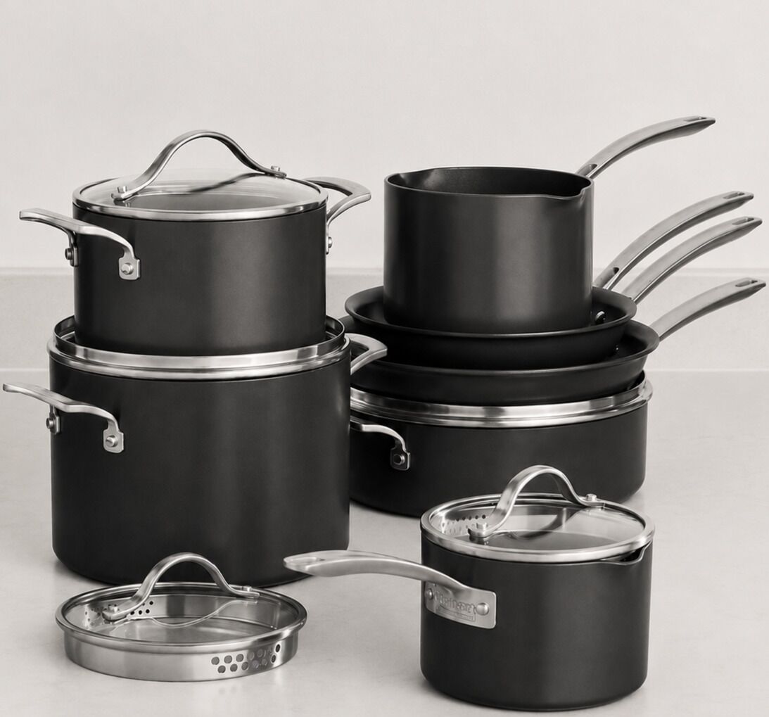A set of black cookware with lids and handles, including a pan, pot, and saucepan.