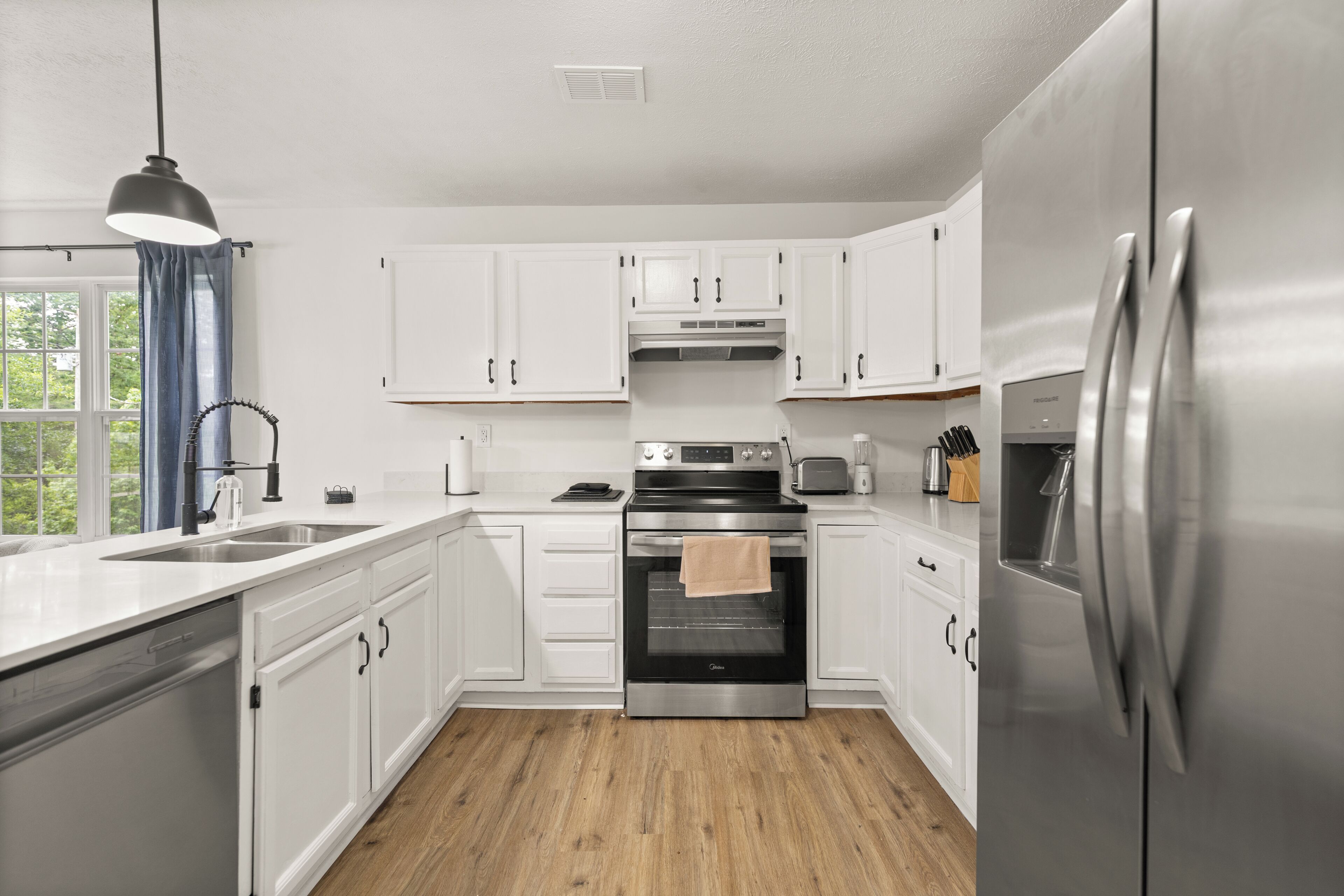 A modern kitchen with white cabinets, stainless steel appliances, and a wooden floor.