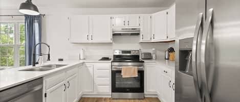 Een moderne keuken met witte kasten, roestvrijstalen apparatuur en een houten vloer.
