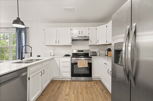 A modern kitchen with white cabinets, stainless steel appliances, and a wooden floor.