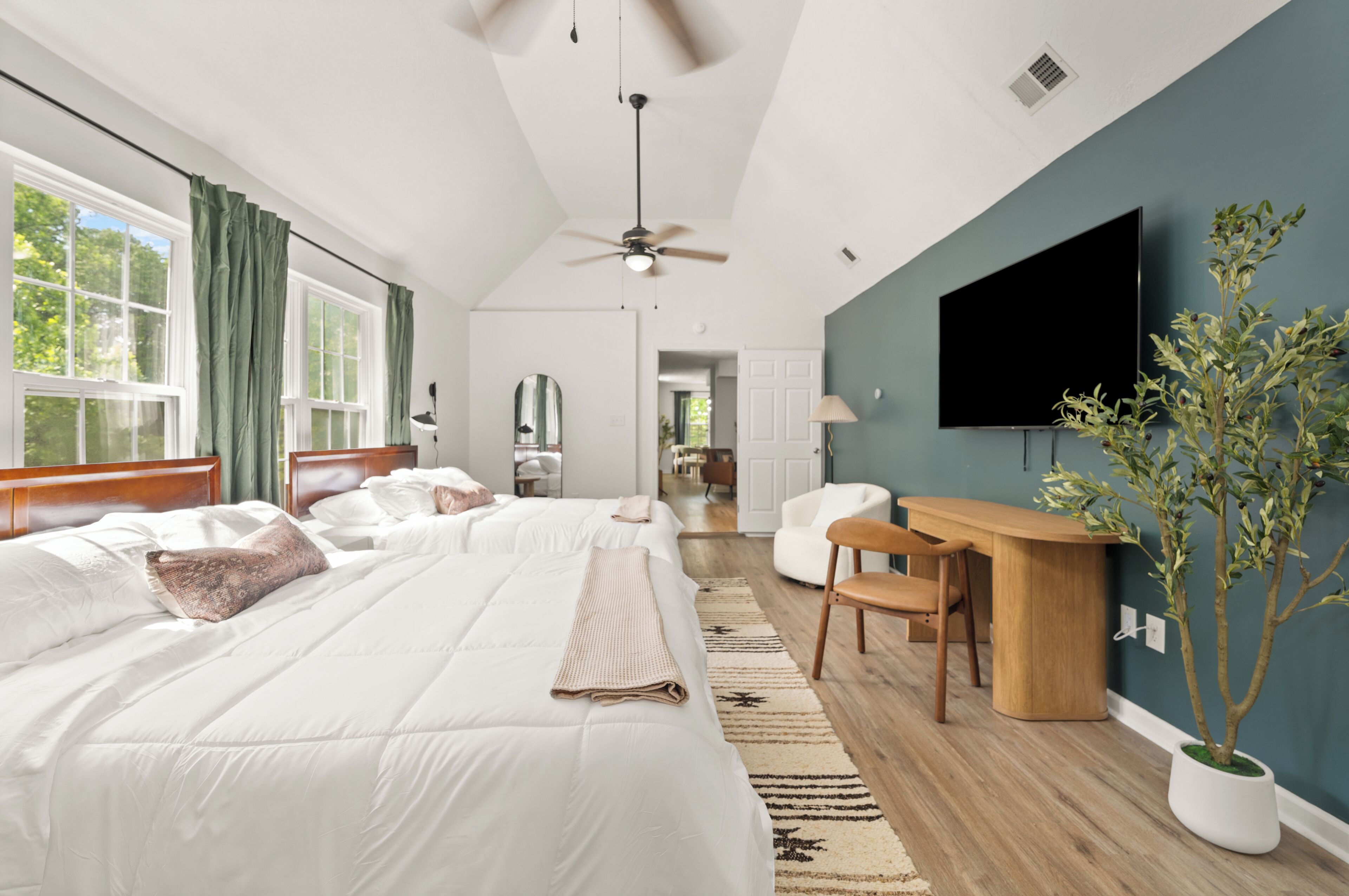 A bedroom with two beds, a desk, a chair, a television, and a potted plant.