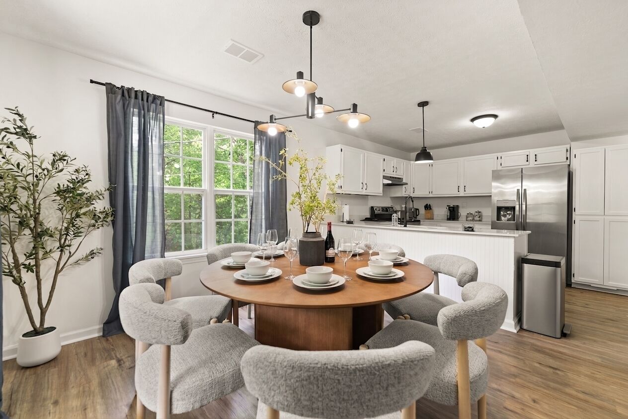 A modern kitchen with white cabinets, a stainless steel refrigerator, and a dining area with a round table and grey chairs.
