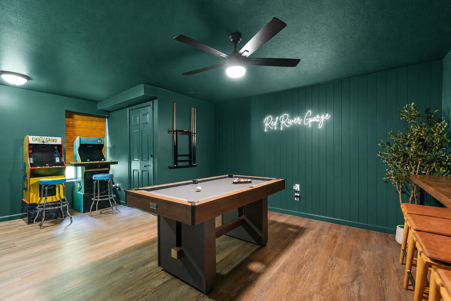 A pool table in a room with green walls, arcade games, and a neon sign.
