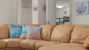 A tan leather sectional sofa with three decorative pillows, a white door, and a wall with artwork. - Guava Ohana 17105-Beach Nearby-Sleeps 11 (Panama City Beach)