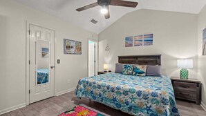 A bedroom with a bed, a nightstand, a lamp, a ceiling fan, and a door. - Guava Ohana 17105-Beach Nearby-Sleeps 11 (Panama City Beach)