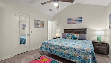 A bedroom with a bed, a nightstand, a lamp, a ceiling fan, and a door.