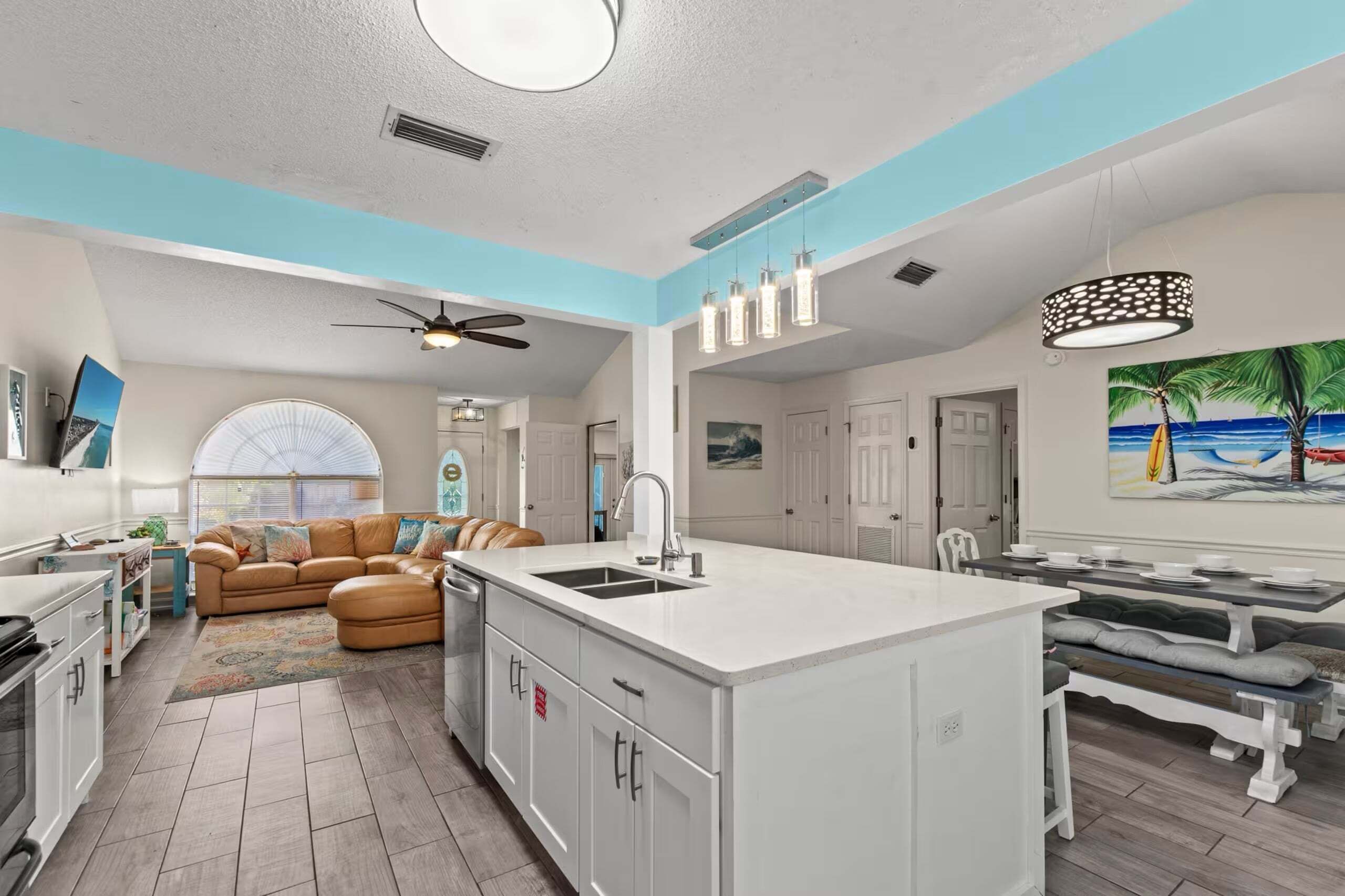 Cozinha moderna com ilha central, área de refeições com mesa e cadeiras e sala de estar com sofá e ventilador.