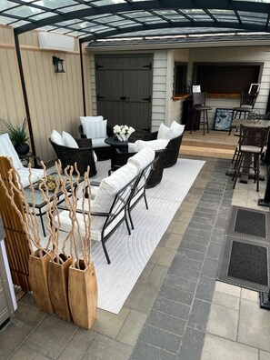 An outdoor patio area with a covered seating area, a dining table, and a large window.
