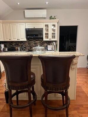 A kitchen with a central island, two bar stools, and a microwave.