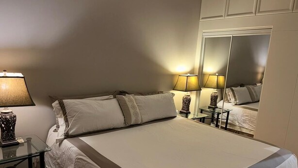 Habitació d'hotel amb un llit gran, làmpades laterals, un mirall i una taula petita amb un ram.