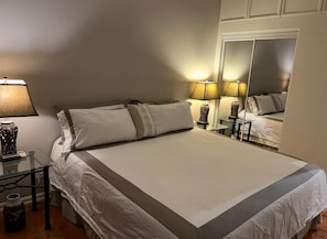 Een hotelkamer met een groot bed, bedlampen, een spiegel en een klein tafeltje met een vaas.