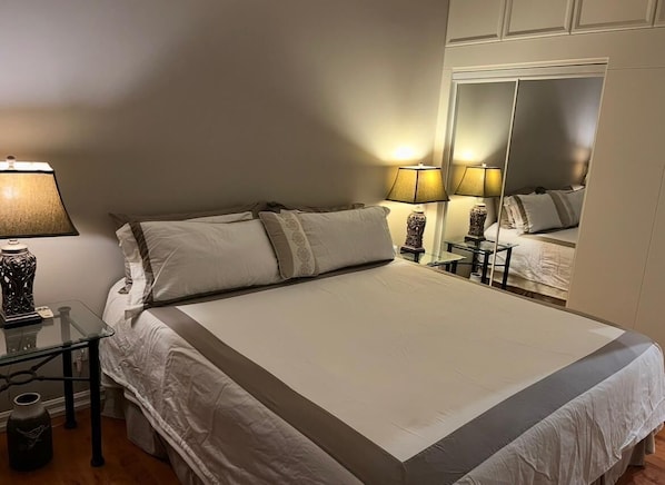 A hotel room with a large bed, bedside lamps, a mirror, and a small table with a vase.