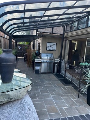 Un patio al aire libre con una parrilla, un cartel de bienvenida y una mesa de vidrio.