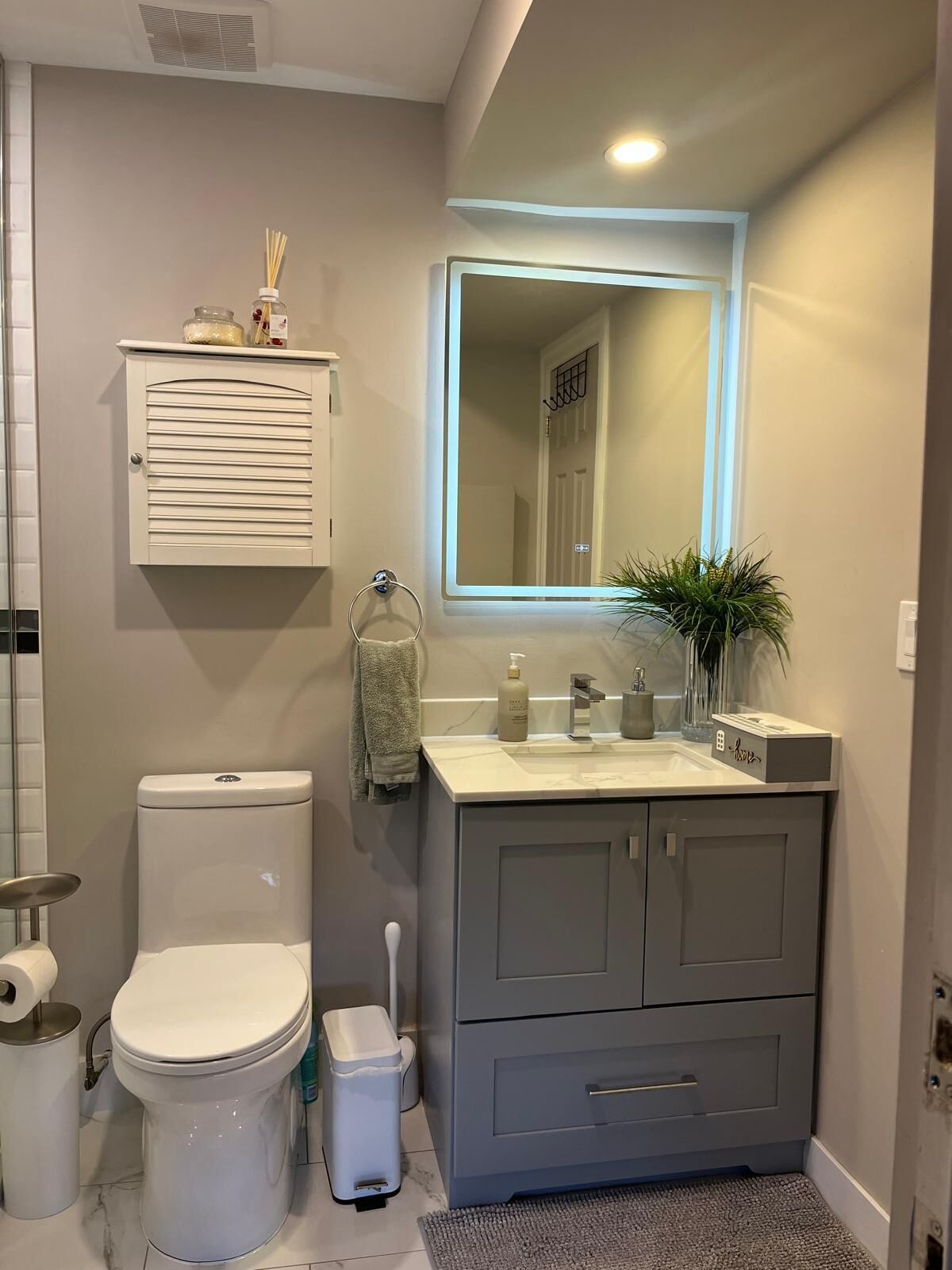 A bathroom with a toilet, sink, mirror, and storage cabinet.