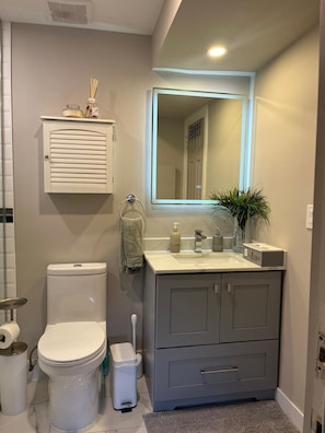 A bathroom with a toilet, sink, mirror, and storage cabinet.