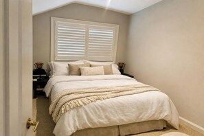 Un dormitorio con una cama, dos mesitas de noche y un ventanal con persianas.