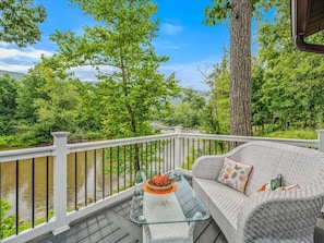 A deck with a wicker sofa and a glass coffee table, overlooking a river and lush greenery. - Welcome to the river - River, Wifi, Deck, Fire Ring (Great Cacapon)