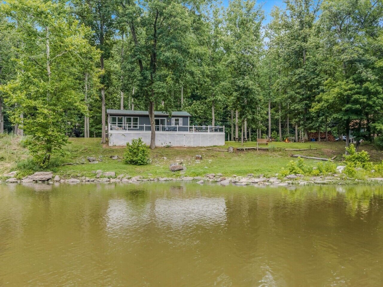 A lakeside cabin with a dock, surrounded by dense trees and a calm body of water.
