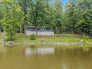 Eine Hütte am Seeufer mit einer Anlegestelle, umgeben von dichtem Wald und ruhigem Wasser.