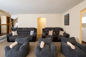 A living room with two dark sofas, a coffee table, and a staircase leading to another level. - 3BR Home w/ Private Cinema • BBQ • Home Office • 10 minutes from Airport (Denver)