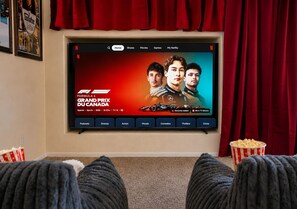 A home theater setup with a large screen displaying a Formula 1 Grand Prix ad, popcorn buckets, and a cozy seating area. - 3BR Home w/ Private Cinema • BBQ • Home Office • 10 minutes from Airport (Denver)