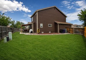 A two-story house with a covered patio, a fenced backyard, and a well-maintained lawn. - 3BR Home w/ Private Cinema • BBQ • Home Office • 10 minutes from Airport (Denver)