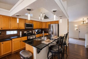 A modern kitchen with wooden cabinets, stainless steel appliances, and a central island with seating. - 3BR Home w/ Private Cinema • BBQ • Home Office • 10 minutes from Airport (Denver)