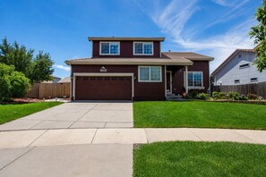 A two-story house with a garage, a well-maintained lawn, and a clear sky. - 3BR Home w/ Private Cinema • BBQ • Home Office • 10 minutes from Airport (Denver)
