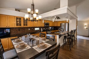 A modern kitchen with wooden cabinets, a central island, stainless steel appliances, and a dining area set for six. - 3BR Home w/ Private Cinema • BBQ • Home Office • 10 minutes from Airport (Denver)