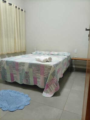 Un lit simple avec une couvre-lit à motifs, une serviette roulée posée sur le lit et une nappe bleue sur le sol.