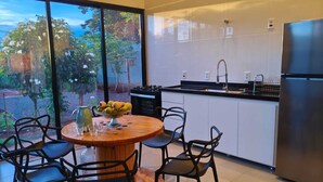 A modern kitchen with a large window, a dining table with chairs, and a refrigerator.