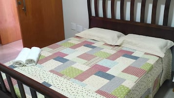 Un lit avec une couette, des oreillers et une tête de lit en bois, dans une pièce dotée d’une porte et d’un interrupteur sur le mur.