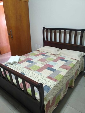 A bed with a quilt, pillows, and a wooden headboard in a room with a door and a light switch on the wall.