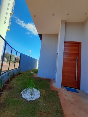 A modern building with a blue exterior, a wooden door, and a small garden area with grass and plants.