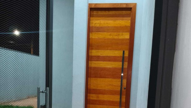 A modern building entrance with a wooden door, a metal gate, and a concrete pathway.