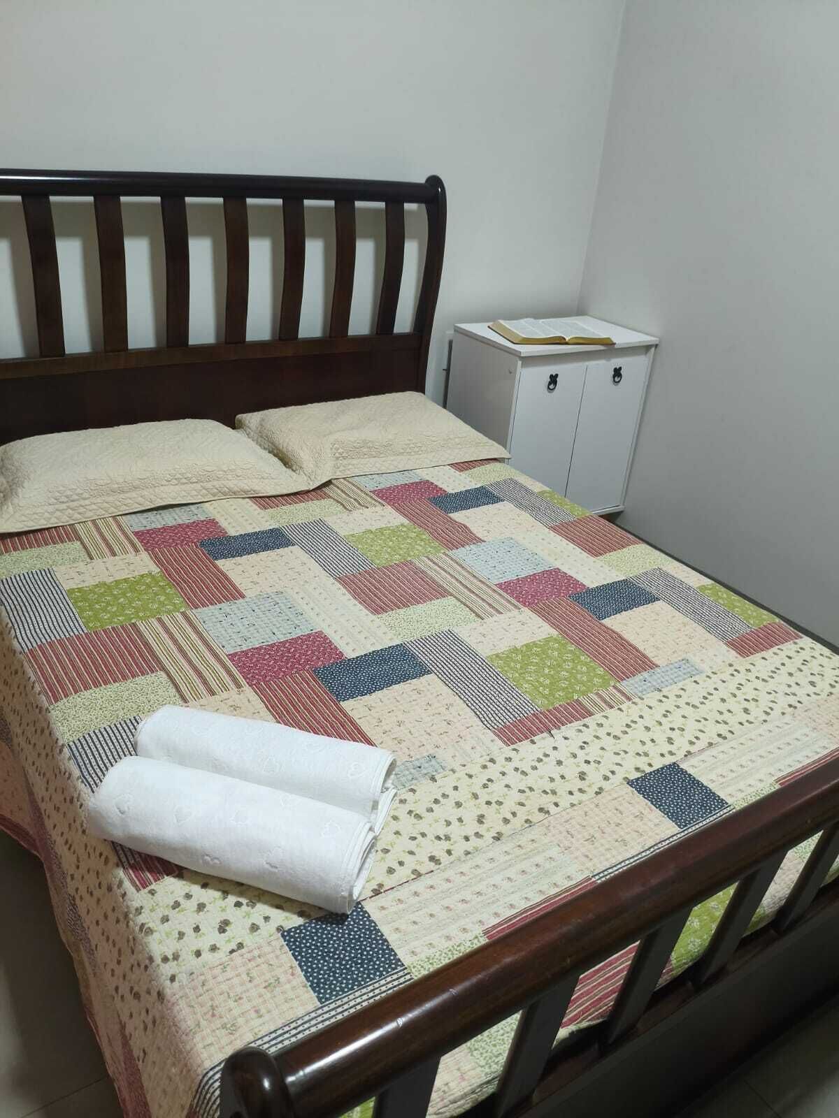 A bedroom with a wooden bed frame, a quilt, and a small white cabinet.