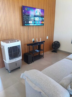Una habitación con una cama, un calentador portátil, un televisor montado en una pared de madera y un ventilador en el suelo.