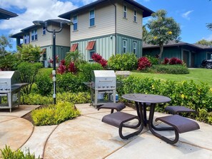 A patio area with outdoor seating and barbecue grills, surrounded by well-maintained landscaping and a building in the background. - Spacious 3BR Garden-Level Villa with Central A/C & Lanai (Koloa)
