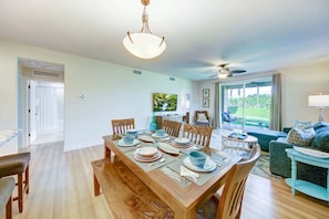 A dining area with a wooden table set for four, surrounded by chairs, with a television and artwork on the wall. - Spacious 3BR Garden-Level Villa with Central A/C & Lanai (Koloa)