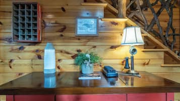 Interieur van een houten blokhut met een houten trap, een Coca-Cola koelkast, een ingelijst certificaat, een lamp, een kleine potplant en een rode kast met metalen handgrepen.