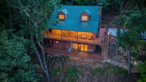 A cabin with a green roof, multiple windows, and a wooden deck.