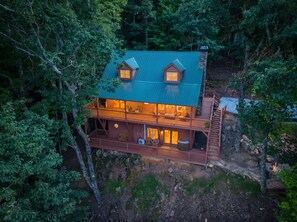 A cabin with a green roof, multiple windows, and a wooden deck.