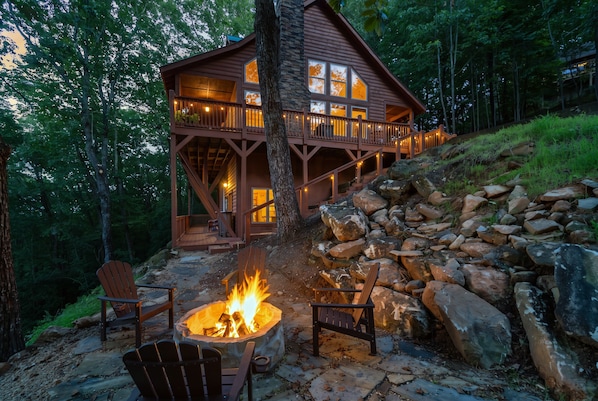A cabin with a stone fire pit and Adirondack chairs.