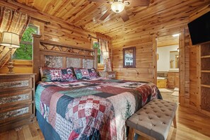 Une chambre dans une cabane en bois, avec un grand lit, un banc et un ventilateur de plafond.