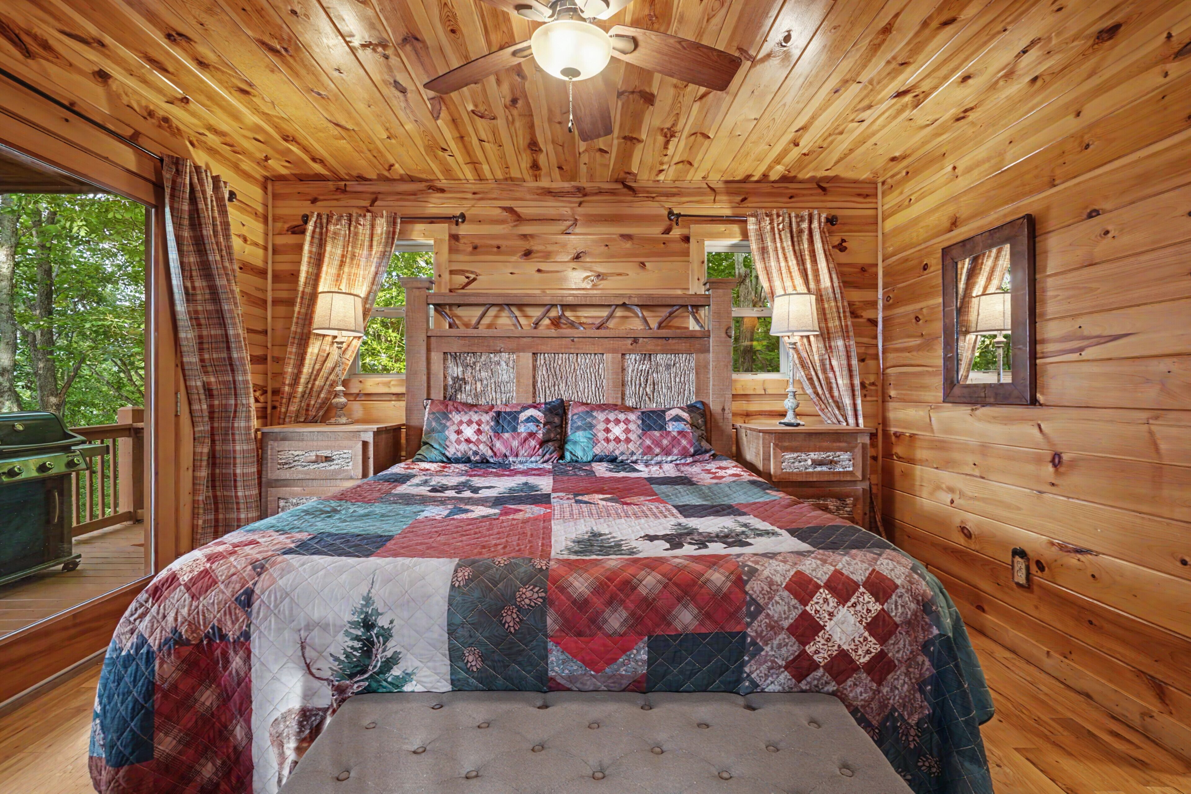 Une chambre située dans un chalet en rondins, avec un grand lit, deux tables de chevet, un ventilateur de plafond et une fenêtre avec des rideaux.