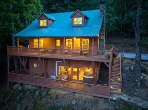 Une cabane en rondins à deux étages, dotée d’un balcon, d’un escalier et d’une véranda.